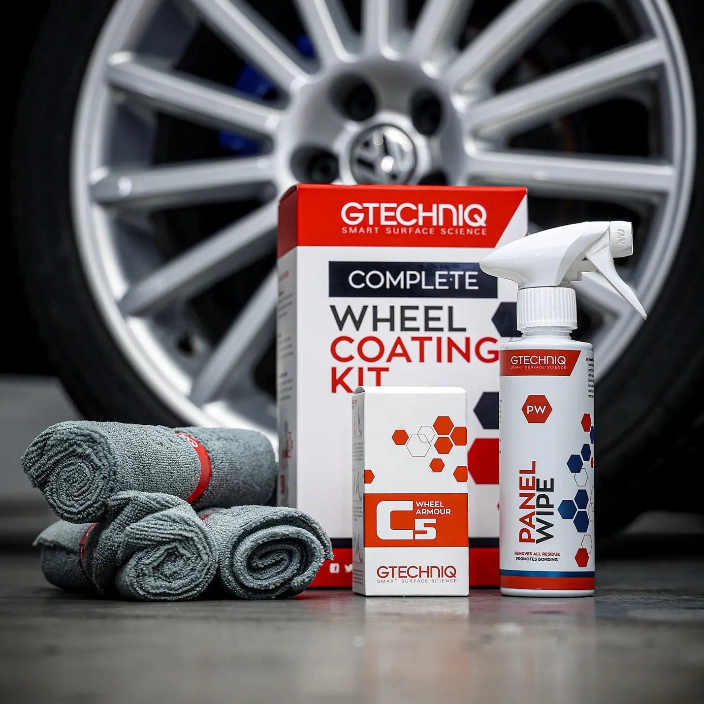 GTechniq car care products including a spray bottle, towels, and packaging in front of a car wheel.