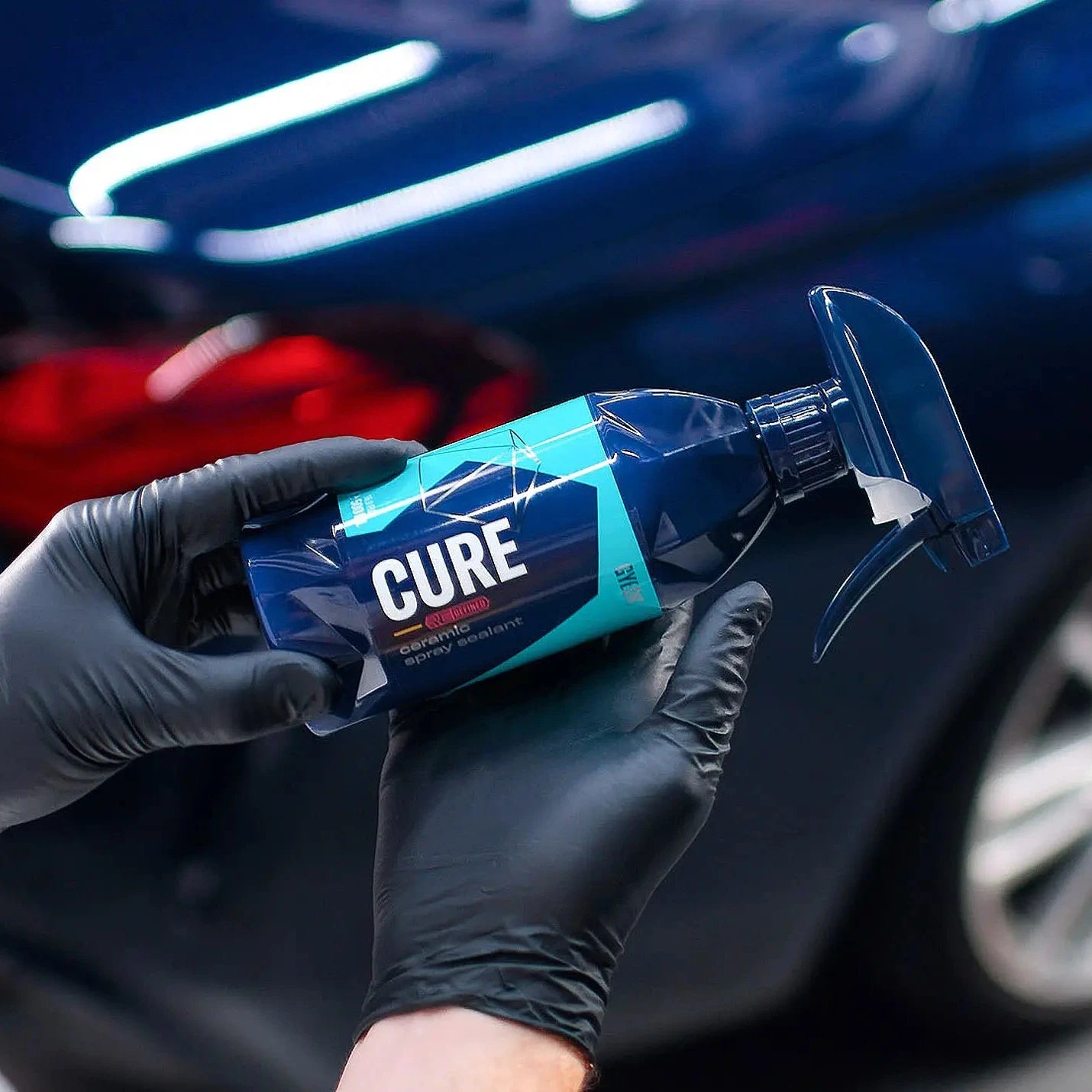 Person holding a 'GYEON CURE' product packaging with a car in the background