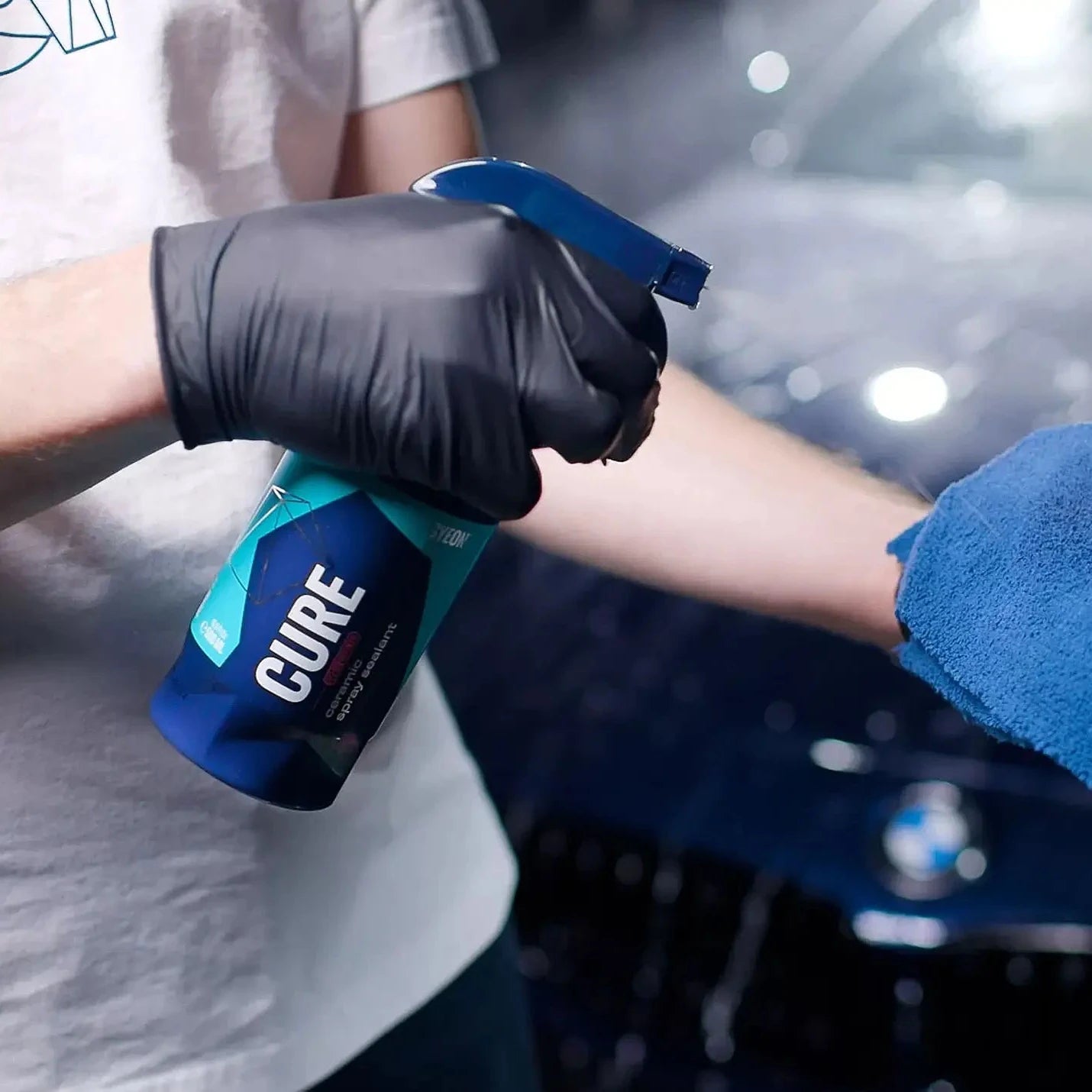 Person applying a product labeled 'GYEON CURE' to a car with a blue towel.
