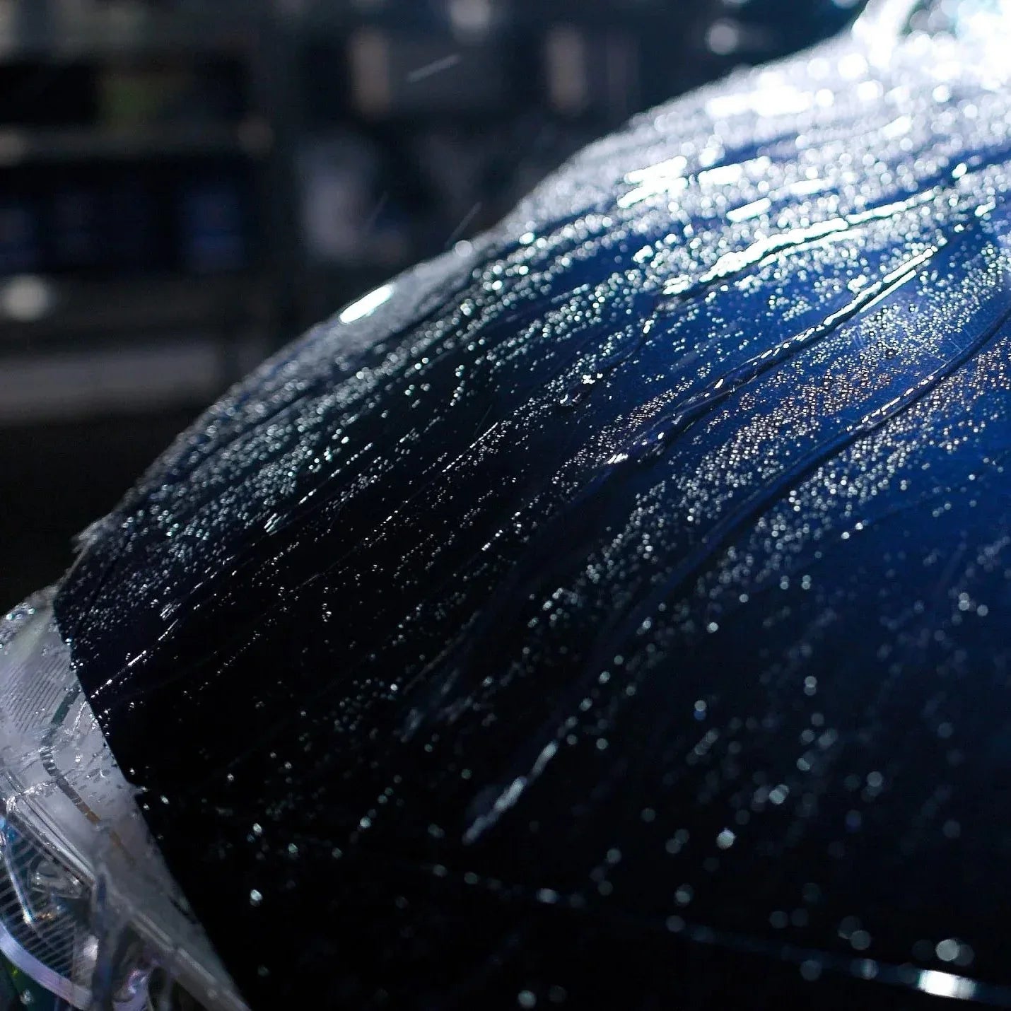 Close-up of a car's hood with water droplets on a blurred background