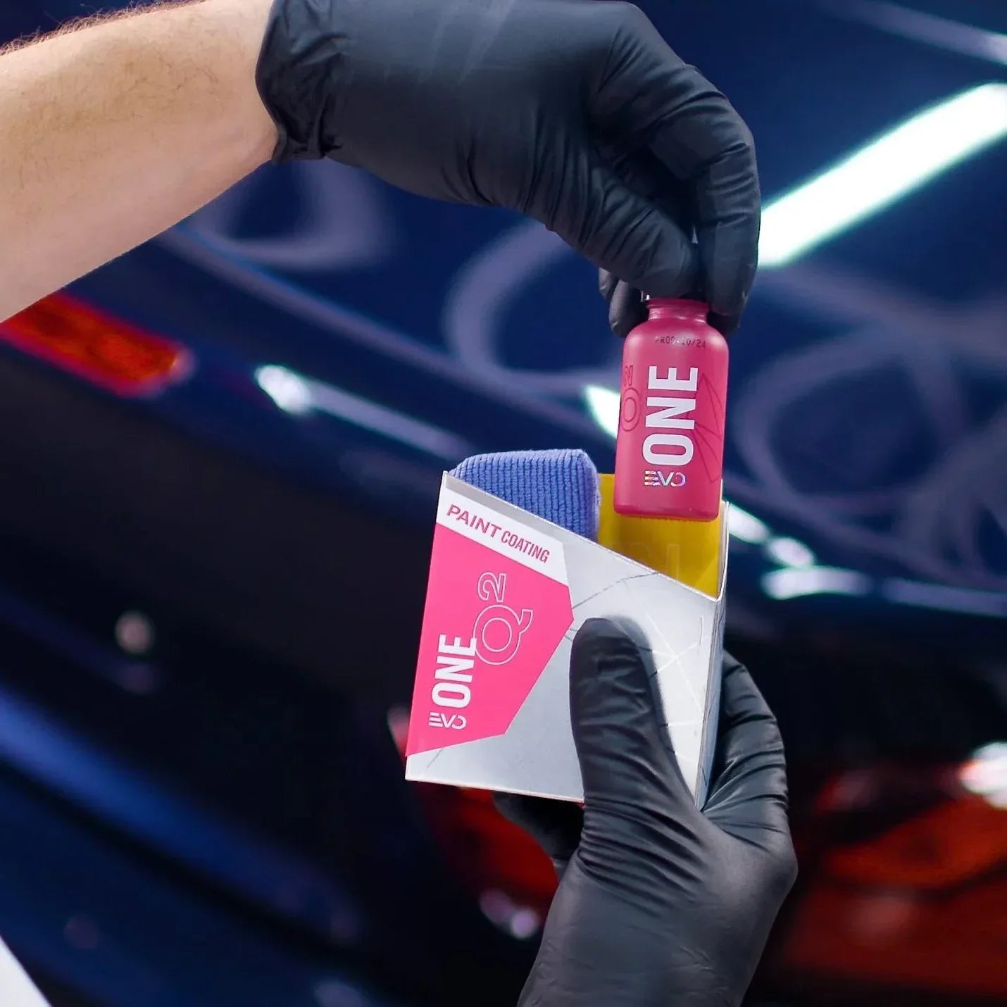 Person holding a 'Gyeon ONE' product with a car in the background