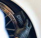 Person wearing a black glove holding a GYEON tyre dressing applicator near a car wheel.