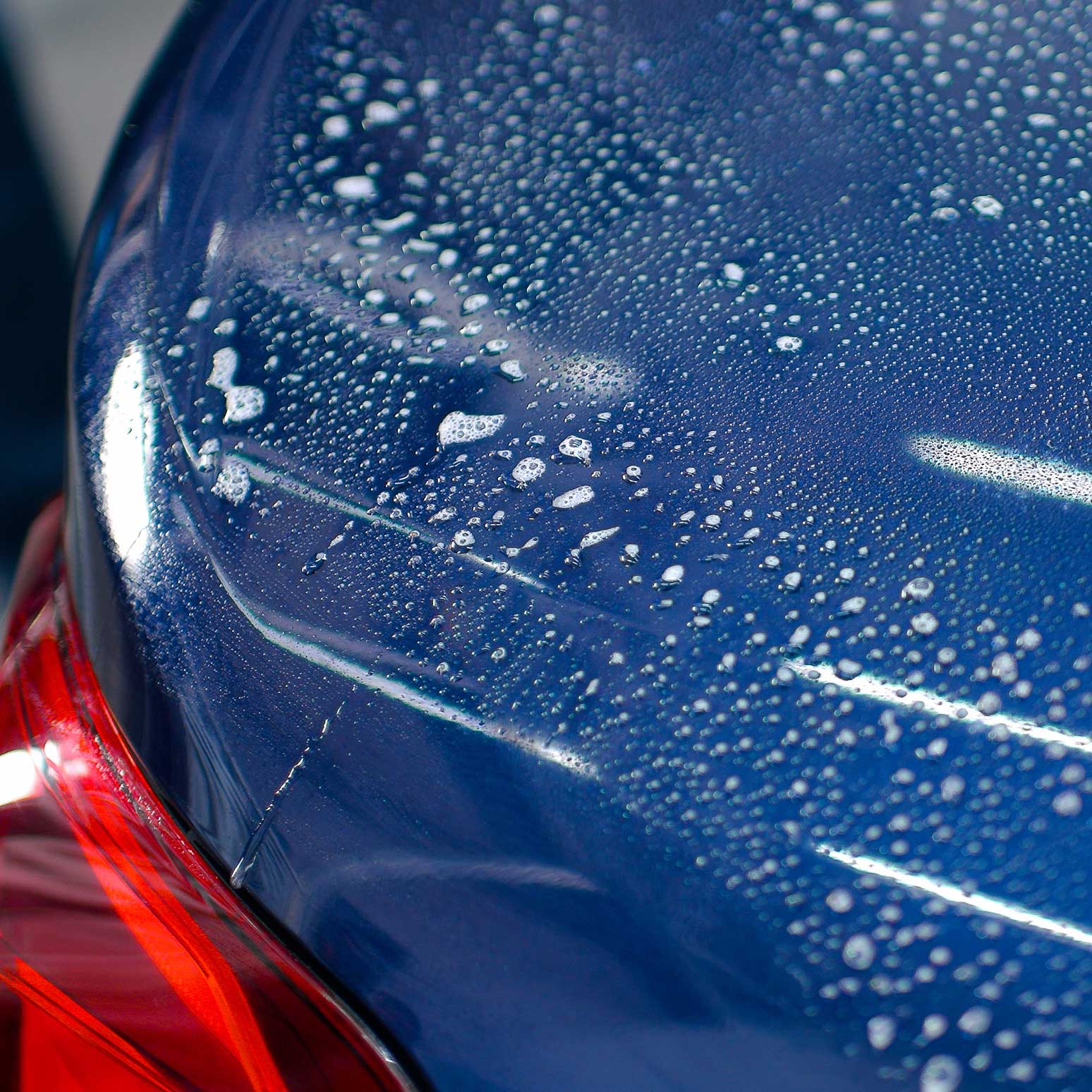 Close-up of a blue car's hood with water droplets