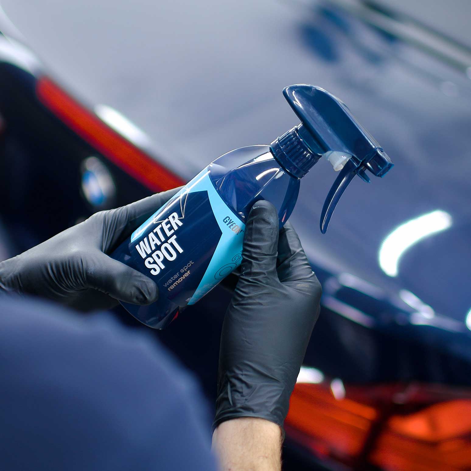 Person holding a bottle of 'Gyeon Water Spot' car cleaning product with a car in the background