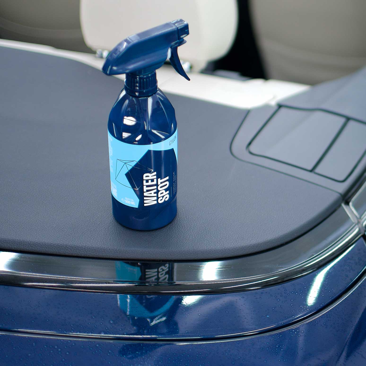 Blue spray bottle labeled 'Gyeon Water Spot Remover' on a car's black dashboard.
