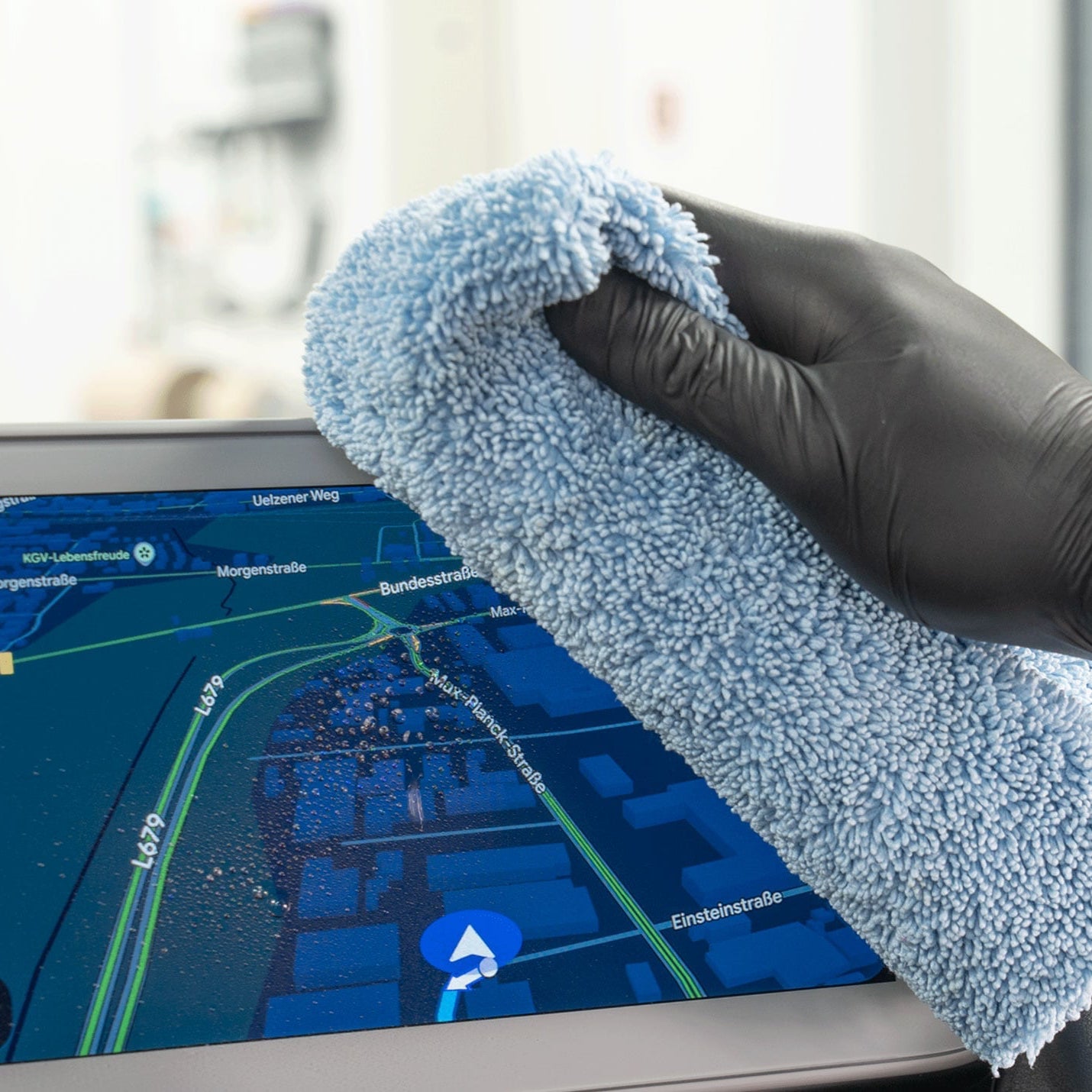 A gloved hand holding a light blue microfiber cleaning cloth in front of a touchscreen device displaying a map.