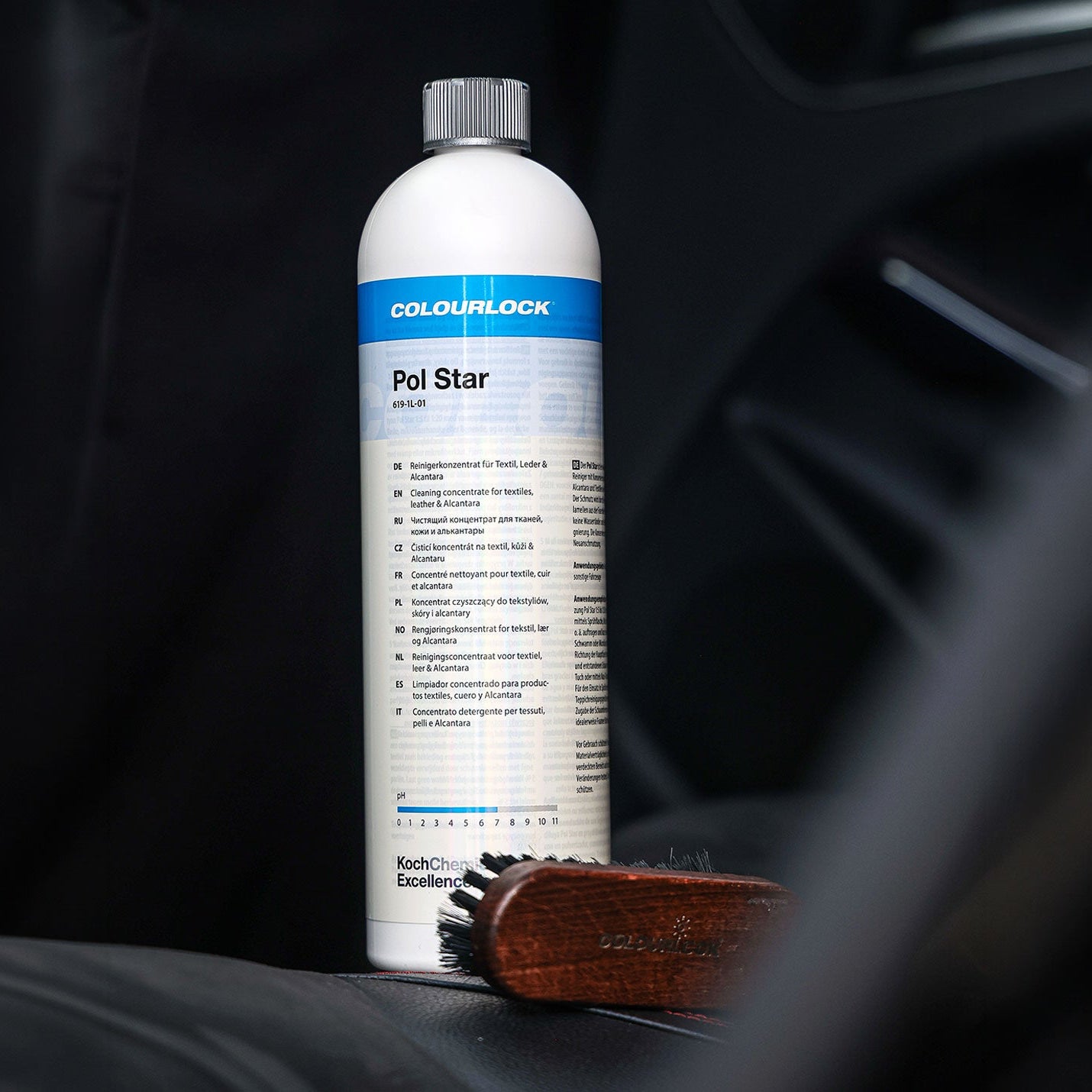 A bottle of Colourlock Pol Star car polish stands on a dark car seat, with a small wooden brush resting beside it. The background is a blurred car interior.