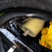 Close-up of a sponge and yellow towel on a car's black surface with water droplets.