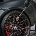 Person cleaning a car wheel with a Sponge Guru Wheel Brush and spray bottle, focusing on the BMW logo.
