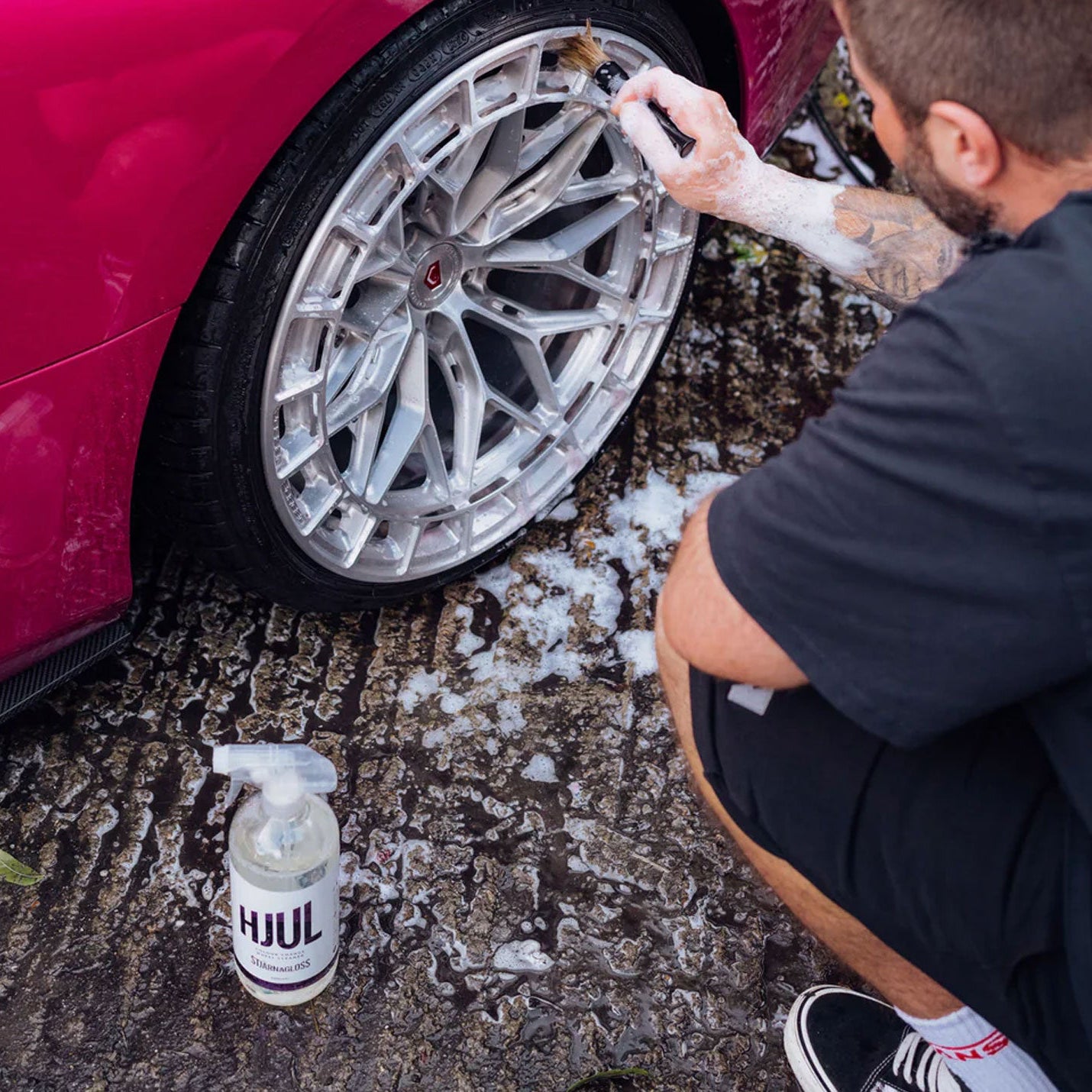 Person cleaning car wheel with a spray bottle of Stjarnagloss Hjul on a textured ground.