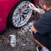 Person cleaning car wheel with a spray bottle of Stjarnagloss Hjul on a textured ground.