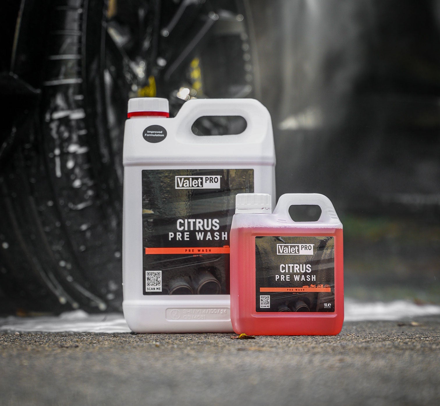 Two bottles of Valet Pro Citrus Pre Wash on a car wash platform with a blurred car tire in the background.