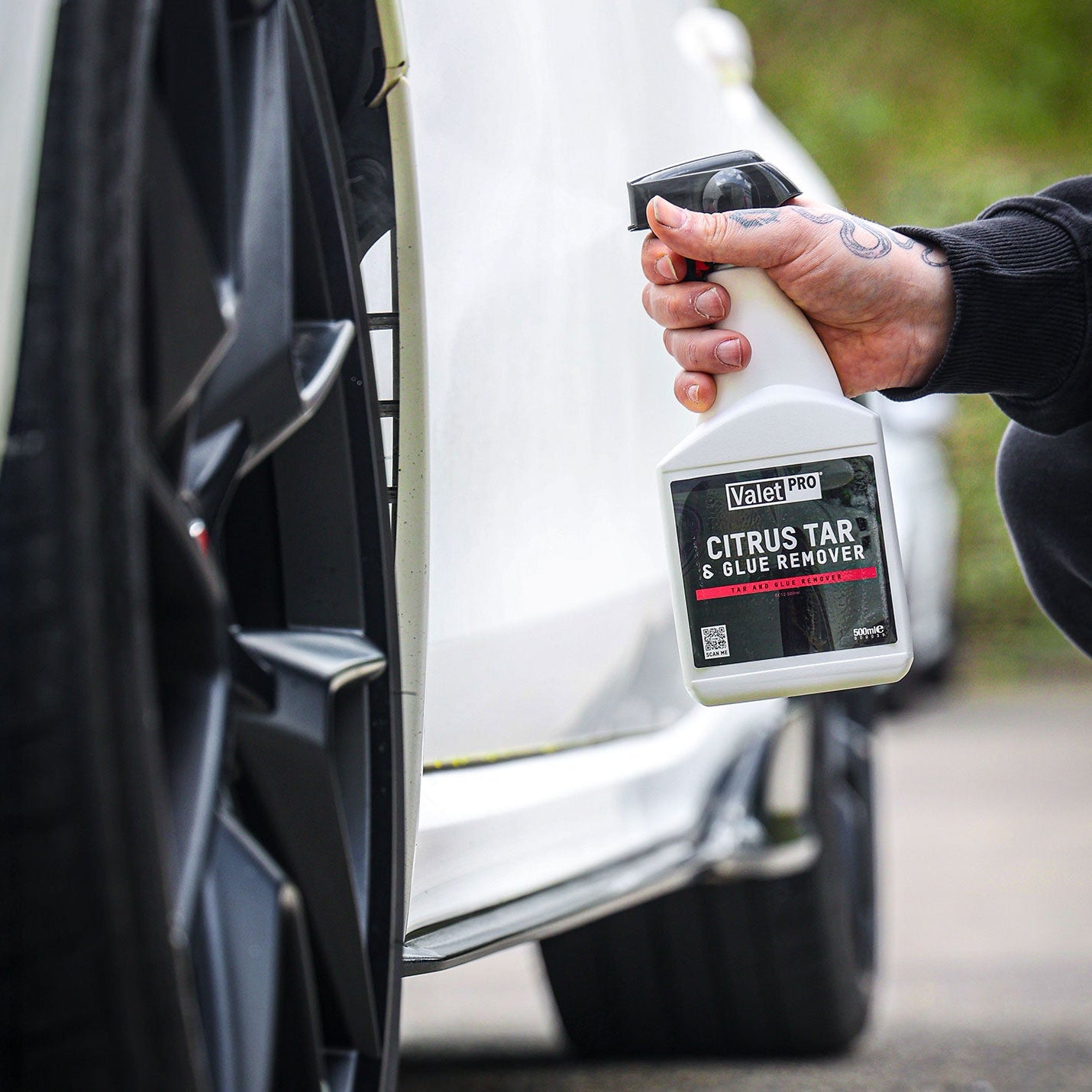 Person holding a bottle of Valmet Citrus Tar & Glue Remover next to a car.